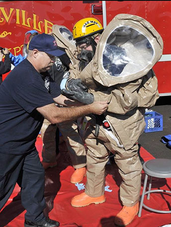 a firefighter helps another into a special suit worn by hazardous materials team members