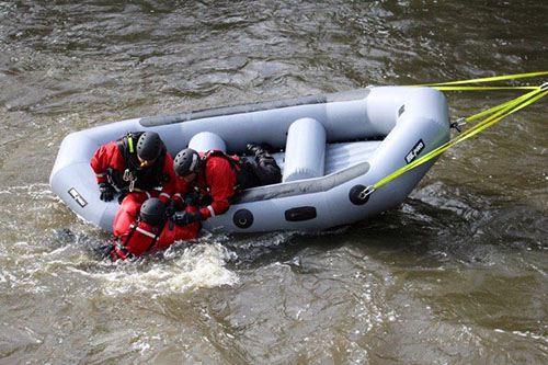 members of the Water Rescue Team pull another member onto an inflatable raft during a training exercise