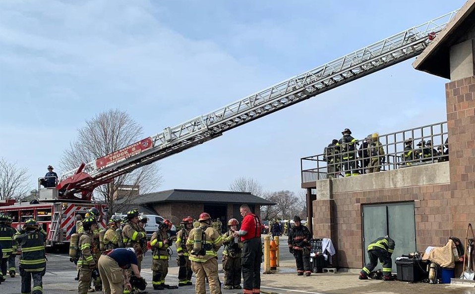 Fire Explorers in training gather around a fire truck with ladder extended to a roof of a nearby building