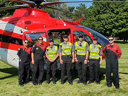 Cadets in safety vests stand next to a medical helicopter