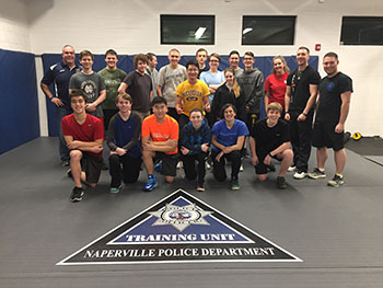 A large group of cadets poses for a photo in NPD's defensive tactics room
