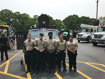 Several cadets volunteering at a community event pose in front of NPD's armored vehicle
