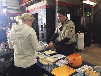 A cadet hands information to a resident from behind a table at the public safety open house