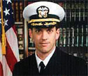 Navy officer Commander Dan Shanower in his uniform in front of an American flag and bookcase