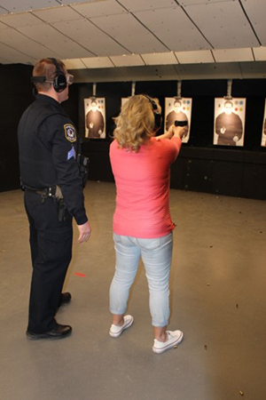 A resident aims a firearm at a target as a training officer observes