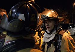 A firefighter speaks to residents wearing firefighter gear