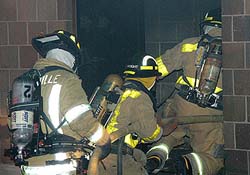 three firefighters in full gear enter a building through a doorway 