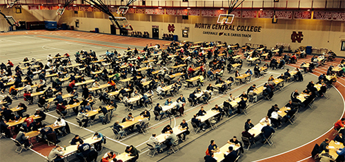 people taking a test at dozens of tables spread out in North Central College's field house