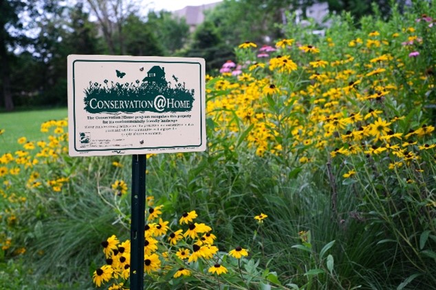 Conservation@Home sign in front of a native garden with pink and yellow flowers