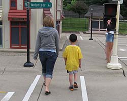 A woman holds a child's hand as they cross a street in a marked crosswalk