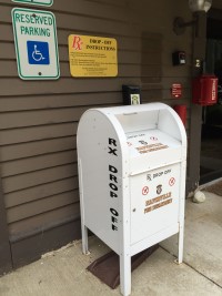 a free-standing mailbox painted white with text: Rx Drop Box outside a Naperville fire station