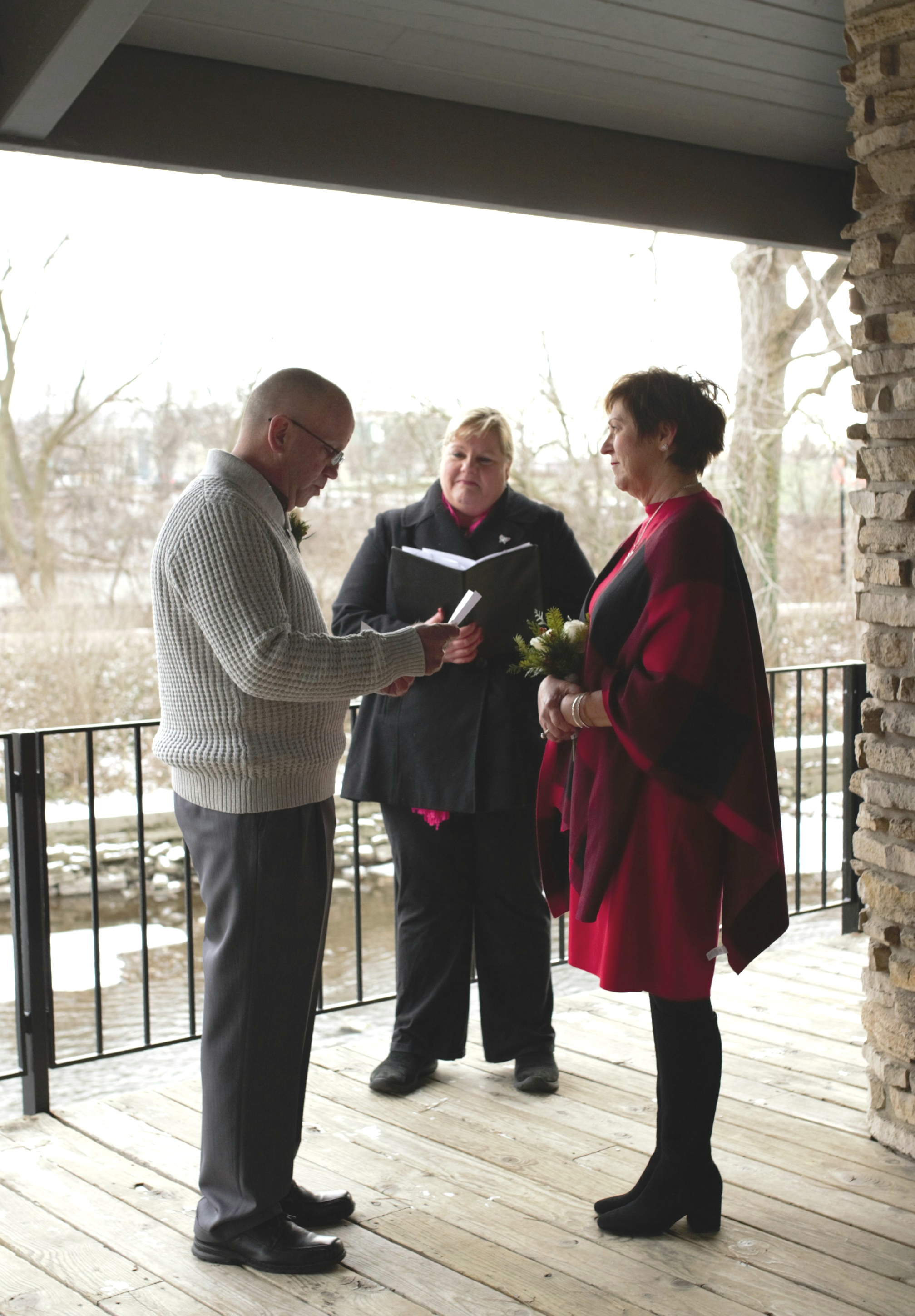 A couple holds hands in a pavilion along the riverwalk as a minister marries them outdoors