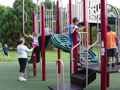 Several children climb on a colorful playground structure while a parent stands nearby.