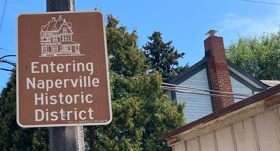A brown-and-white sign with an image of a Victorian home tells visitors they are entering Naperville's historic district.